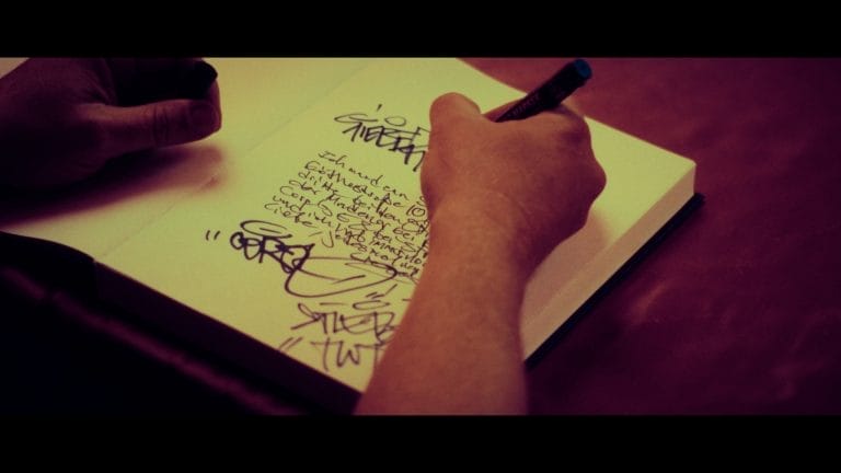 Szene aus dem Musikvideo, in der die Deutschrapper in ein Buch unterschreiben.